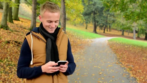 Man op telefoon (bericht schrijven) - man glimlach (gelukkig) - man in de herfst park (aard) — Stockvideo