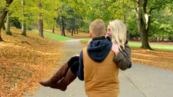 Joven modelo pareja enamorada - parque de otoño (naturaleza) - hombre lleva a una mujer en sus brazos - feliz pareja - disparado desde la espalda — Vídeo de stock