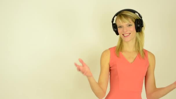 Young attractive woman listens to music with headphones and woman welcomes - studio — Stock Video