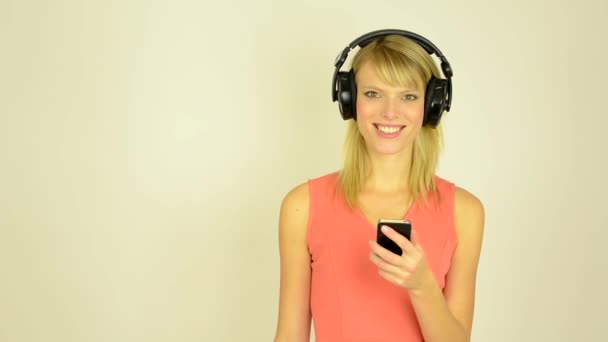 Young attractive woman listens to music with headphones with phone - studio - woman look to the phone and camera — Stock Video