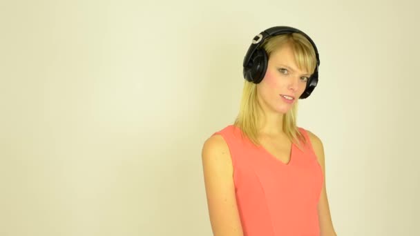 Mulher atraente jovem ouve música com fones de ouvido e mulher tem um olhar sedutor - estúdio — Vídeo de Stock