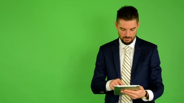 Business man works on tablet and smiles to camera - green screen - studio — Stock Video