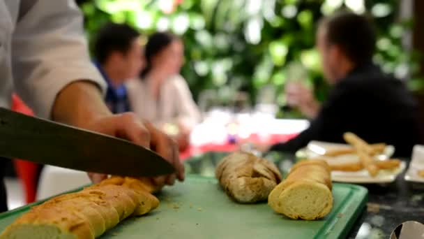Koch kocht - Koch schneidet Baguette (Brot) - die Leute essen im Hintergrund — Stockvideo