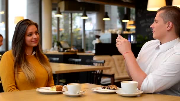 Hombre fotografiando mujer con teléfono inteligente en la cafetería - café y pastel — Vídeo de stock