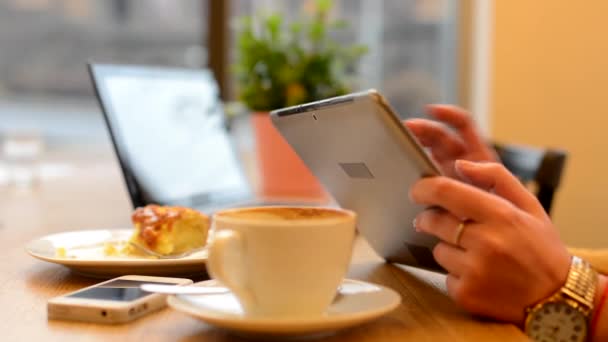 Donna lavora su tablet in caffè - girato a portata di mano - computer, smartphone caffè e torta in background - strada urbana con auto in background — Video Stock