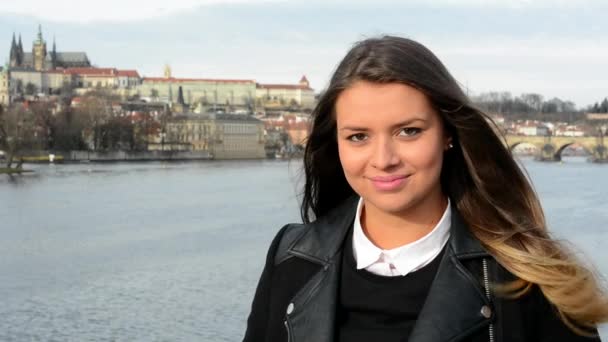 Jovem mulher atraente sorrisos - ponte - cidade (Praga) no fundo - close-up — Vídeo de Stock