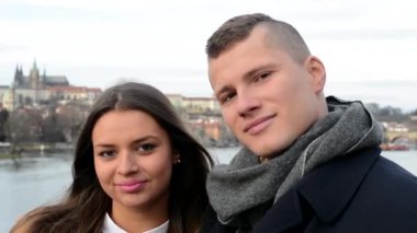 Aşık genç mutlu çift öpücük ve kamera - city (Prag) arka plan - portre için gülümse