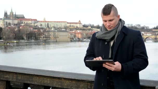 El hombre trabaja en la tableta en el puente - ciudad (Praga) en el fondo — Vídeos de Stock