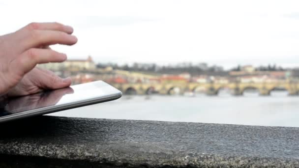 Man arbetar på tablett på bron - staden (Prag) och floden i bakgrunden - närbild (skott å) — Stockvideo