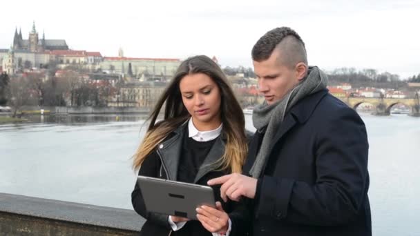 Feliz pareja de trabajo en la tableta en el puente - ciudad (Praga) en segundo plano — Vídeos de Stock