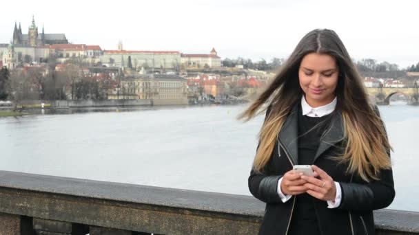 Kobieta pracuje na smartphone i uśmiecha się do kamery na moście - miasto (Praga) w tle — Wideo stockowe