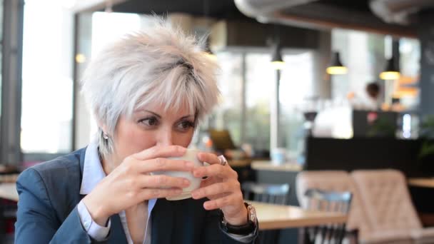 Business middle aged woman drinks coffee in cafe and smiles to camera - closeup — Stock Video