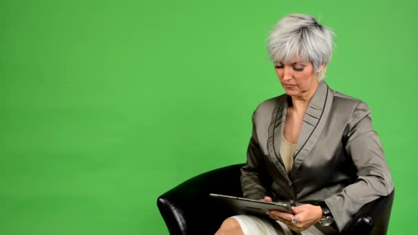 Business middle aged woman sits and works on tablet - green screen - studio — Stock Video