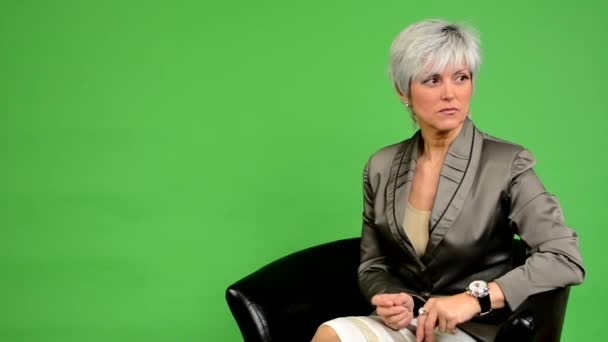 Деловая женщина средних лет сидит и ждет (смотрит на часы) и листья - зеленый экран - студия — стоковое видео