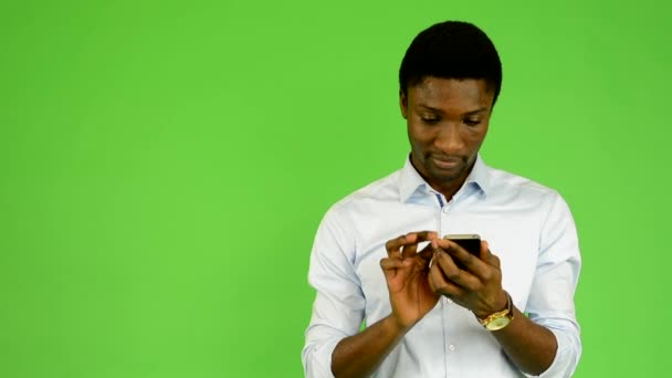 Joven hombre negro guapo trabaja en el teléfono inteligente y sonrisas - pantalla verde - estudio — Vídeo de stock