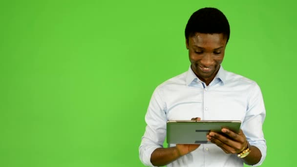 Jovem homem negro bonito trabalha em tablet e sorrisos - tela verde - estúdio — Vídeo de Stock