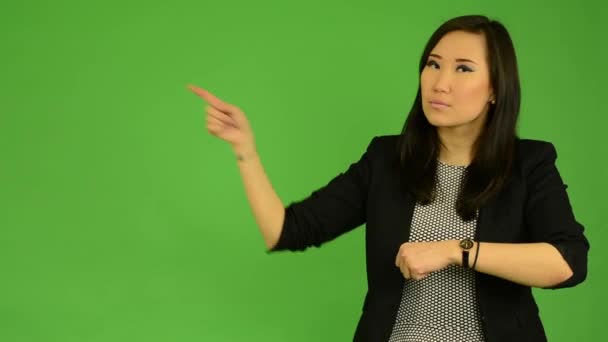 Junge attraktive asiatische Frau zeigt auf die Uhr - green screen studio — Stockvideo