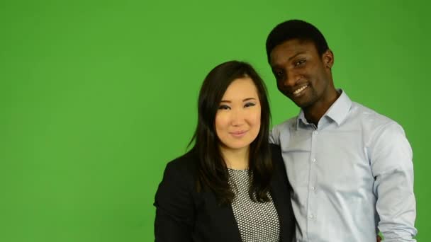 Happy couple kiss and smile to camera - black man and asian woman - green screen studio — Stock Video