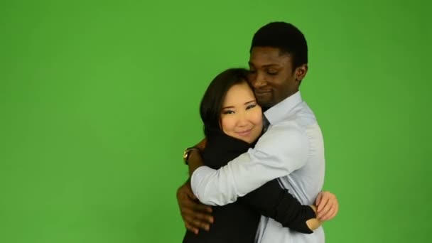 Boldog pár szerelmes ölelés és csók és mosoly a kamera - fekete férfi és ázsiai nő - zöld képernyő stúdió — Stock videók