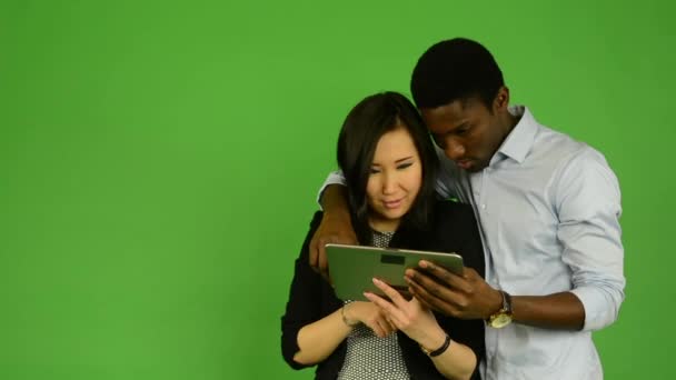 Feliz pareja trabajo en tablet y sonrisa a cámara - negro hombre y asiático mujer - verde pantalla estudio — Vídeo de stock