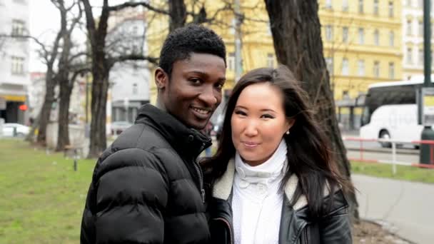 Щаслива пара посміхається до камери - чорний чоловік і азіатка - міська вулиця з машиною - місто — стокове відео