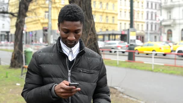 Молодой красивый черный мужчина работает на смартфоне - городская улица с автомобилями - город — стоковое видео