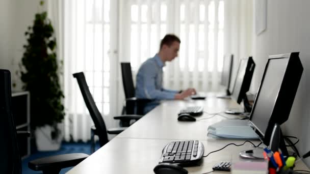 Jonge knappe man werkt op desktop computer in het kantoor - op de achtergrond — Stockvideo