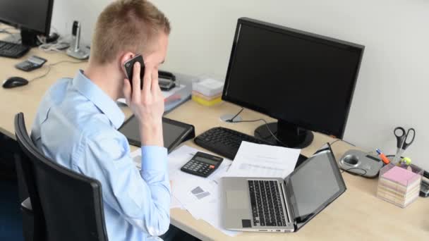 Mladý pohledný muž sedí a pracuje na stolním počítači v kanceláři a telefonu — Stock video