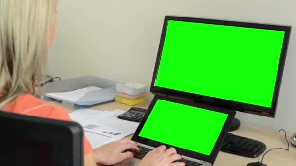 Junge attraktive Frau arbeitet am Laptop und Desktop-Computer im Büro - grüner Bildschirm — Stockvideo