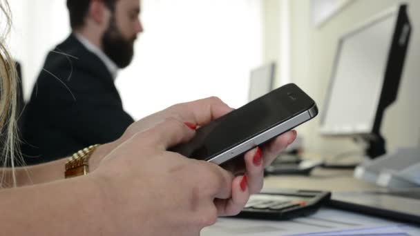 Vrouw werkt op smartphone (closeup) en man werkt op desktop computer in het kantoor — Stockvideo