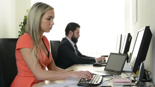 Vrouw wijst naar camera en man werkt op desktop computer in het kantoor — Stockvideo