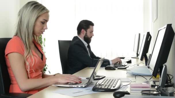 Γυναίκα εργάζεται σε φορητό υπολογιστή και ο άνθρωπος εργάζεται σε επιτραπέζιο υπολογιστή στο γραφείο (εργαζόμενοι) — Αρχείο Βίντεο