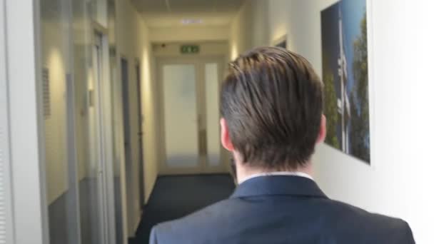 Young handsome man with full-beard (hipster) walks in the office - steadicam - shot from back — Stock Video