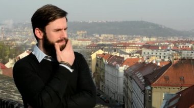 Sakallı, genç ve yakışıklı bir adam. Etrafına bir bak. Arka planda şehir var.