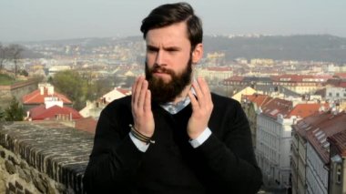 Sakallı genç yakışıklı adam (hipster) yüzünü kollarla kapatır ve sonra şaşırır - arka planda şehir