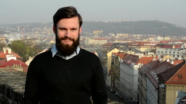 Joven hombre guapo con barba llena (hipster) sonríe a la cámara - ciudad — Vídeo de stock