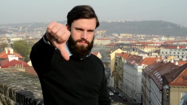 Młody przystojny mężczyzna z pełną brodą (hipster) pokazuje kciuk na odrzucenie - miasto w tle — Wideo stockowe