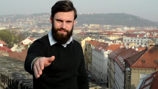 Młody przystojny mężczyzna z pełną brodą (hipster) pomaga w powitaniu - miasto w tle — Wideo stockowe