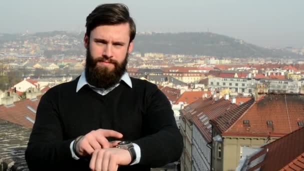 Młody przystojny mężczyzna z pełną brodą (hipster) punkt do oglądania (czas) - miasto w tle — Wideo stockowe