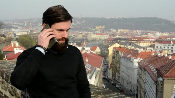 Jovem homem bonito com telefone de barba cheia (hipster) - cidade no fundo — Vídeo de Stock