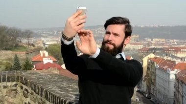 Sakallı (hipster) genç ve yakışıklı bir adam arka planda fotoğraf çekiyor.