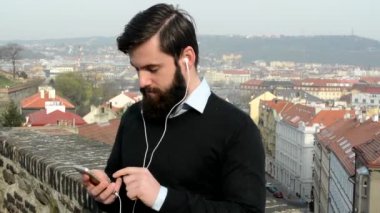 Sakallı genç yakışıklı adam (hipster) Akıllı telefonlu müzik dinle - arka planda şehir