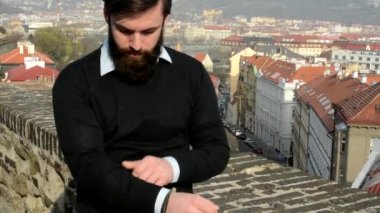 Sakallı genç yakışıklı adam (hipster) giysileri ayarlar - arka planda şehir