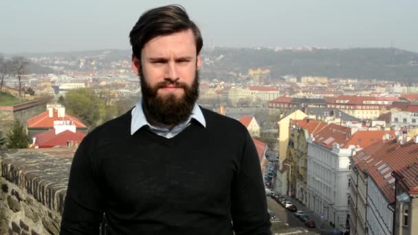 Joven hombre guapo con barba llena (hipster) habla con la cámara y está de acuerdo - ciudad en el fondo — Vídeos de Stock