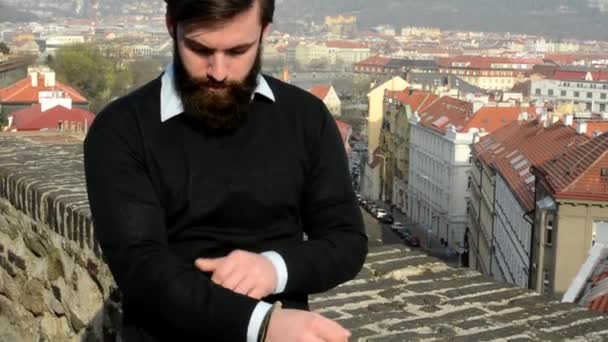 Young handsome man with full-beard (hipster) adjusts clothes - city in background — Stock Video