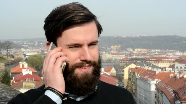 Joven hombre guapo con la barba llena (hipster) teléfono - ciudad en el fondo - primer plano — Vídeos de Stock