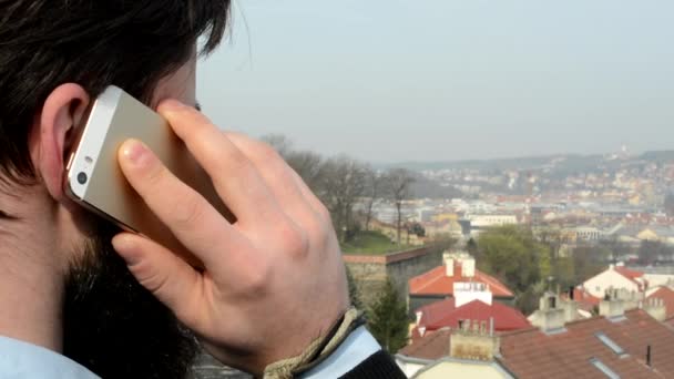 Jonge knappe man met full-bard (hipster) telefoon - stad op de achtergrond - schot van achteren — Stockvideo