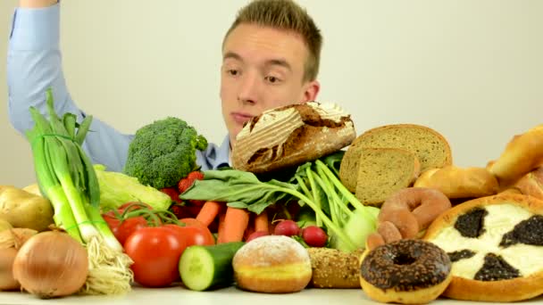 Man choosing between healthy (Vegetables and fruits) food and unhealthy food (baked goods) - right choice is healthy food - white background studio — Stock Video