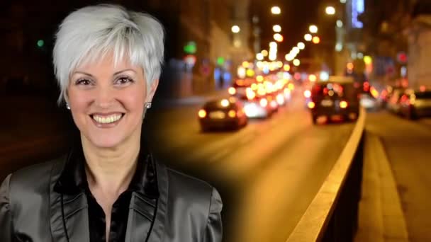 Business middle aged woman smiles - night city - night street with cars - lamps - car headlight - soft blurred - timelapse — Stock Video