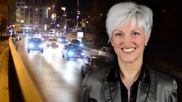 Negócios mulher de meia-idade sorrisos - cidade noturna - rua urbana noite com carros - farol do carro - timelapse — Vídeo de Stock